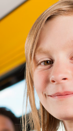 Ein junges Mädchen steht neben einer Haltestange in einem Bus und guckt in die Kamera. Im Hintergrund sind ein Mann mit einem weiteren jungen Mädchen zu sehne. 