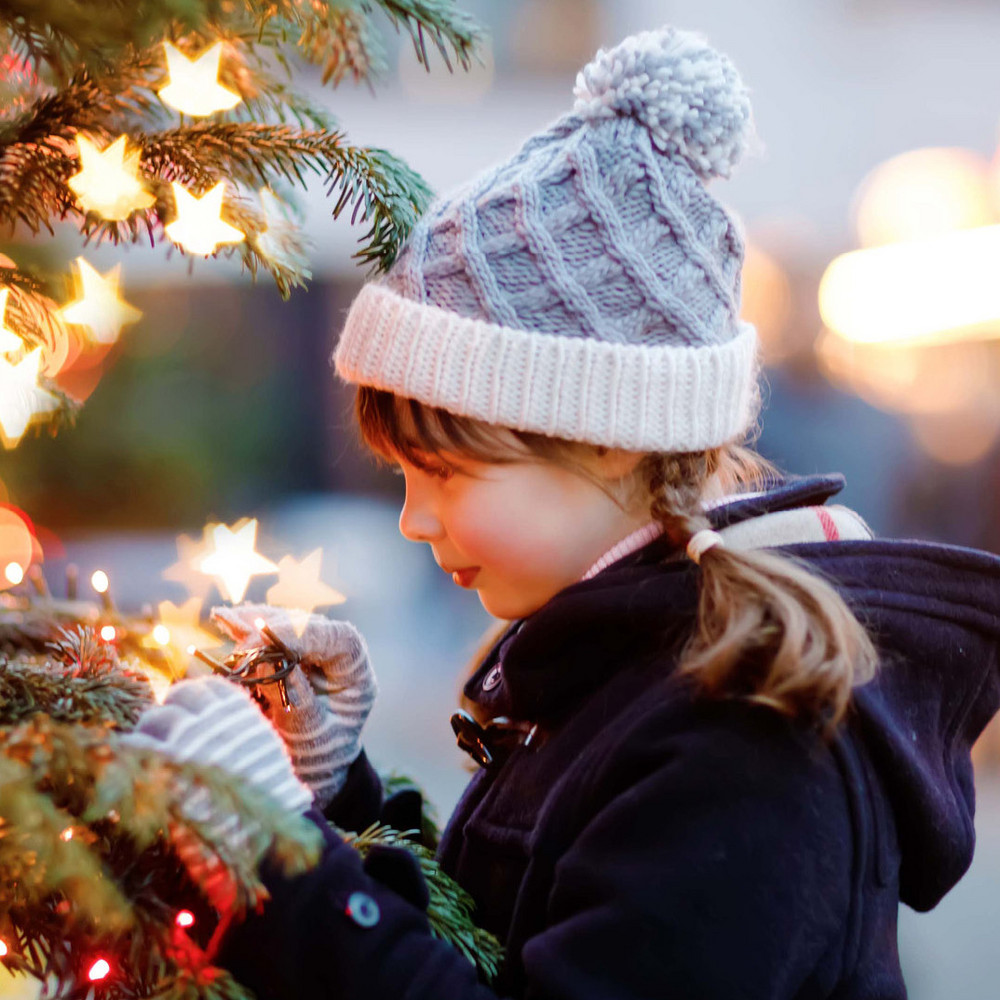 Ein Mädchen steht im Freien vor einem Weihnachtsbaum und hält eine Lichtkette