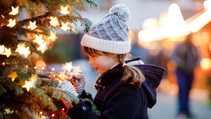 Ein Mädchen steht vor einem Weihnachtsbaum auf einem Weihnachtsmarkt